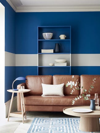 Living space with rich blue (Mazarine) wall and a contrasing neutral (Cool Arbour) stripe  with a tan leather sofa.