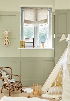 Children's nursery painted in 3 different shades of green neutral 'Green Stone' with children's toys and a small wicker chair.