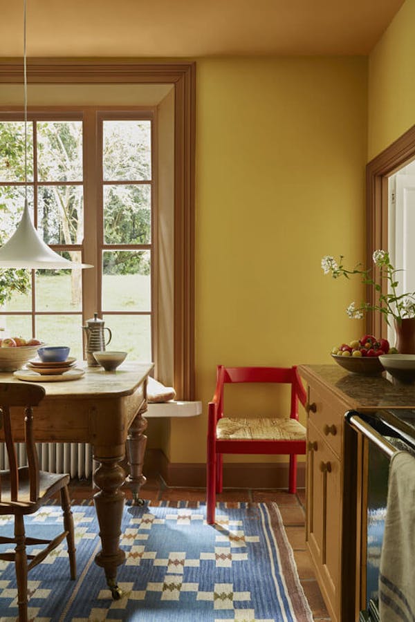 Kitchen painted in rich yellow shade 'Yellow-Pink' with deep gold 'Affogato' on the window frame, mid gold 'Middle Buff' on the ceiling and a bright red chair.