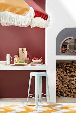 Outside dining area with deep red walls (Arras), a pizza oven, counter and a parasol umbrella.