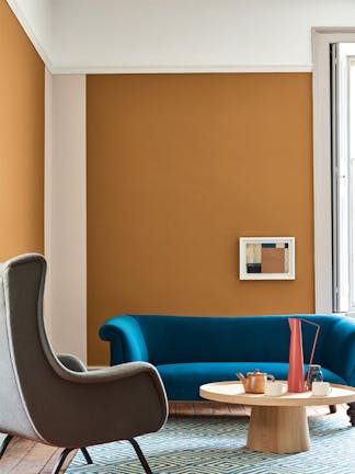 Living space painted in dark orange (Middle Buff) with a contrasting deep blue sofa, grey armchair and wooden table on a rug.