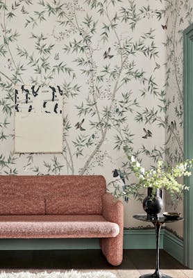 Living room with an off-white bird print mural wallpaper (Belton Scenic - Oyster) with a pink sofa and small table.