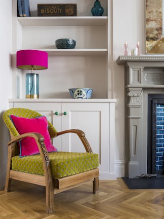 A corner in a living room with a grey built-in bookcase, green and brown chair and the edge of a dark grey fireplace.