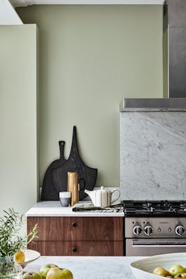 Grey green (Normandy Grey) painted kitchen area with oven, counter, wooden drawers and a set of chopping boards.