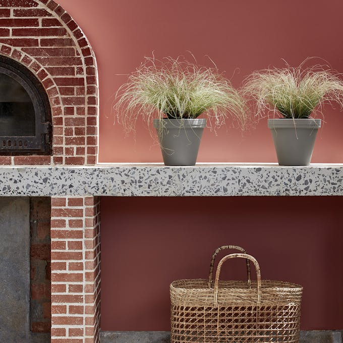 Outdoor kitchen painted in deep terracotta red 'Tuscan Red' with brickwork, plants and a basket.