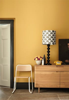 Hallway painted in mustard yellow (Yellow-Pink) with a wooden side table and chair.