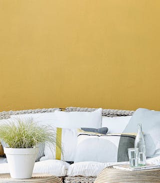 Outside seating area with a large cushioned wicker sofa and chair with a bright yellow wall (Yellow-Pink).