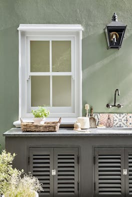 Outside kitchen sink area in grey green 'Boringdon Green' with a contrasting grey cabinet and white window frame.