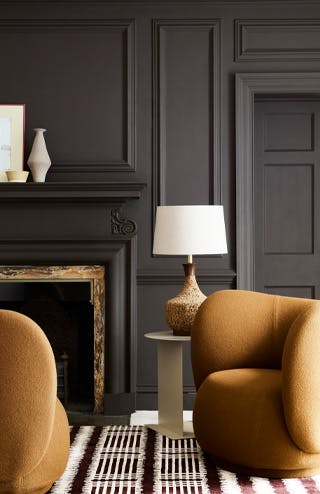 Close-up of a deep brown paneled wall painted in Chocolate Color with two contrasting mustard yellow armchairs in front.