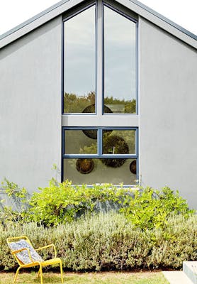 House exterior with large windows painted in mid grey (Urbane Grey) with bright yellow garden chair and plants.