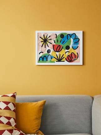 Bright yellow (yellow-pink) wall featuring colorful abstract artwork in a white frame, with grey sofa and cushions in front.