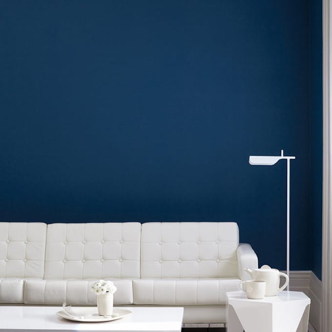 Living room painted in dark blue (Royal Navy) with a white sofa, lamp, table and wooden floor.