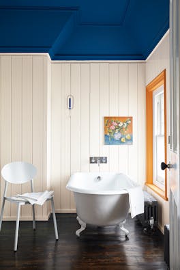 Bathroom with paneled off-white (Flint) walls and a contrasting deep blue ceiling with a bathtub and chair by the window.