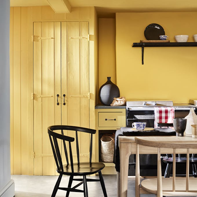 Kitchen color drenched in vibrant yellow shade 'Giallo', with a wooden table and chairs.