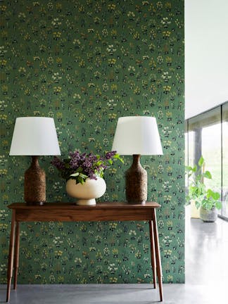 Hallway with green small floral wallpaper 'Millefleur - Garden' and a wooden sidetable with 2 lamps and a vase of flowers.