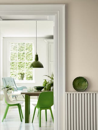 Hallway looking into a dining room painted in beige shade Portland Stone - Dark with bright green dining room chairs.