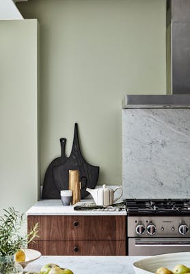 Grey green (Normandy Grey) painted kitchen area with oven, counter, wooden drawers and a set of chopping boards.