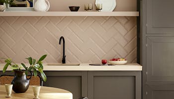 Kitchen painted in muted pink shade 'Mochi' with contrasting neutral brown 'Attic II' units with a dining room table and chair.