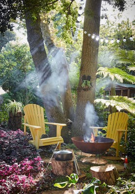 Forest with two bright yellow garden chairs (Giallo) with a barbeque lit surrounded by trees.