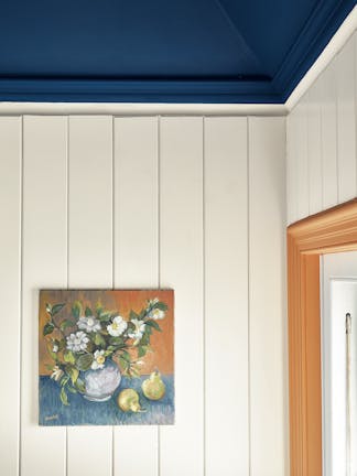 Close-up of a paneled off-white wall painted in Flint, with a flower painting hung up, and a contrasting deep blue ceiling.