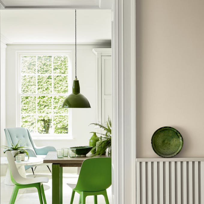 Hallway looking into a dining room painted in beige shade Portland Stone - Dark with bright green dining room chairs.