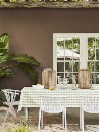 Outside dining table and chairs with the back wall painted in rich chocolate shade 'Scullery' with white panelled doors and a large plant.