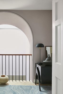 Hallway area painted in different shades of warm neutral China Clay under a large arch with a side table and bannister.