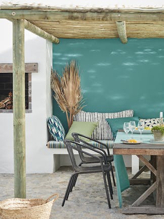 Outdoor table and chairs under a bamboo roof with the back wall painted in blue-green shade 'Canton'.