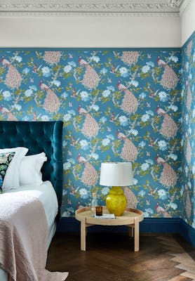 Bedroom with a blue bird print wallpaper (Pavona - Silvie) and a small wooden table next to the bed.