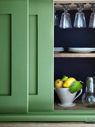 Close-up of deep green kitchen cupboards painted in 'Garden', and partly open revealing two lemons and glassware inside.