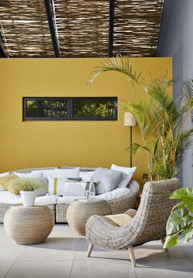 Outside seating area with a large wicker sofa and chair with a bright yellow wall (Yellow-Pink).