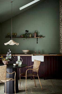 Kitchen with a soft green back wall (Windmill Lane) and aubergine purple (Cordoba) kitchen cabinets with a table and chairs.