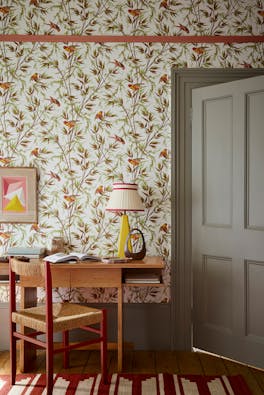 Home study space featuring bird and leaf wallpaper (Great Ormond St - Galette) with a grey door, wooden desk and chair.