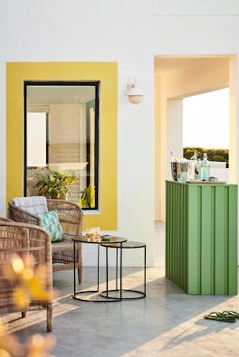 Outside bar in bright green (Garden) with wicker chairs, a drinks table and white walls with Indian Yellow highlights.